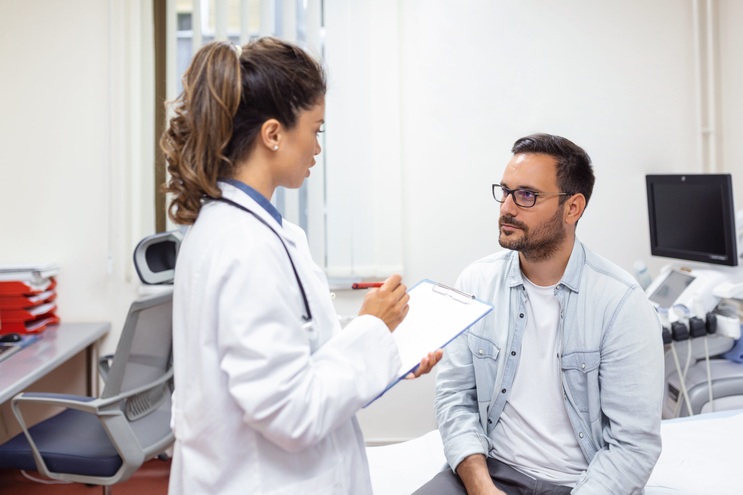 serious man consulting with young female physician doctor at checkup meeting in hospital. skilled general practitioner giving healthcare medical advices to patient.